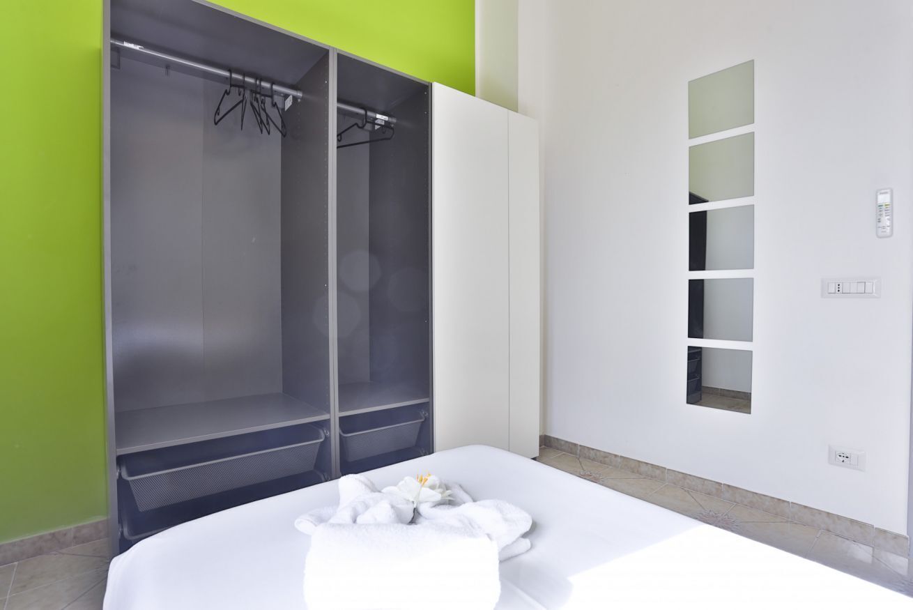 Ein Hotelzimmer mit einem Bett, einem Kleiderschrank, einem Spiegel und einer wandmontierten Bedienkonsole.