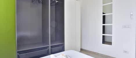 Et hotelværelse med en seng, et klædeskab, et spejl og et panel til styring på væggen.