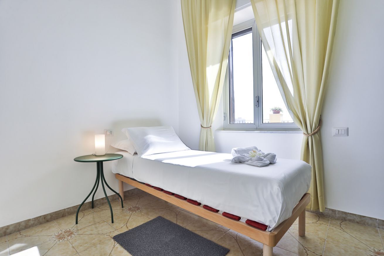 A single bed with a wooden frame, a bedside table with a lamp, and a window with curtains.