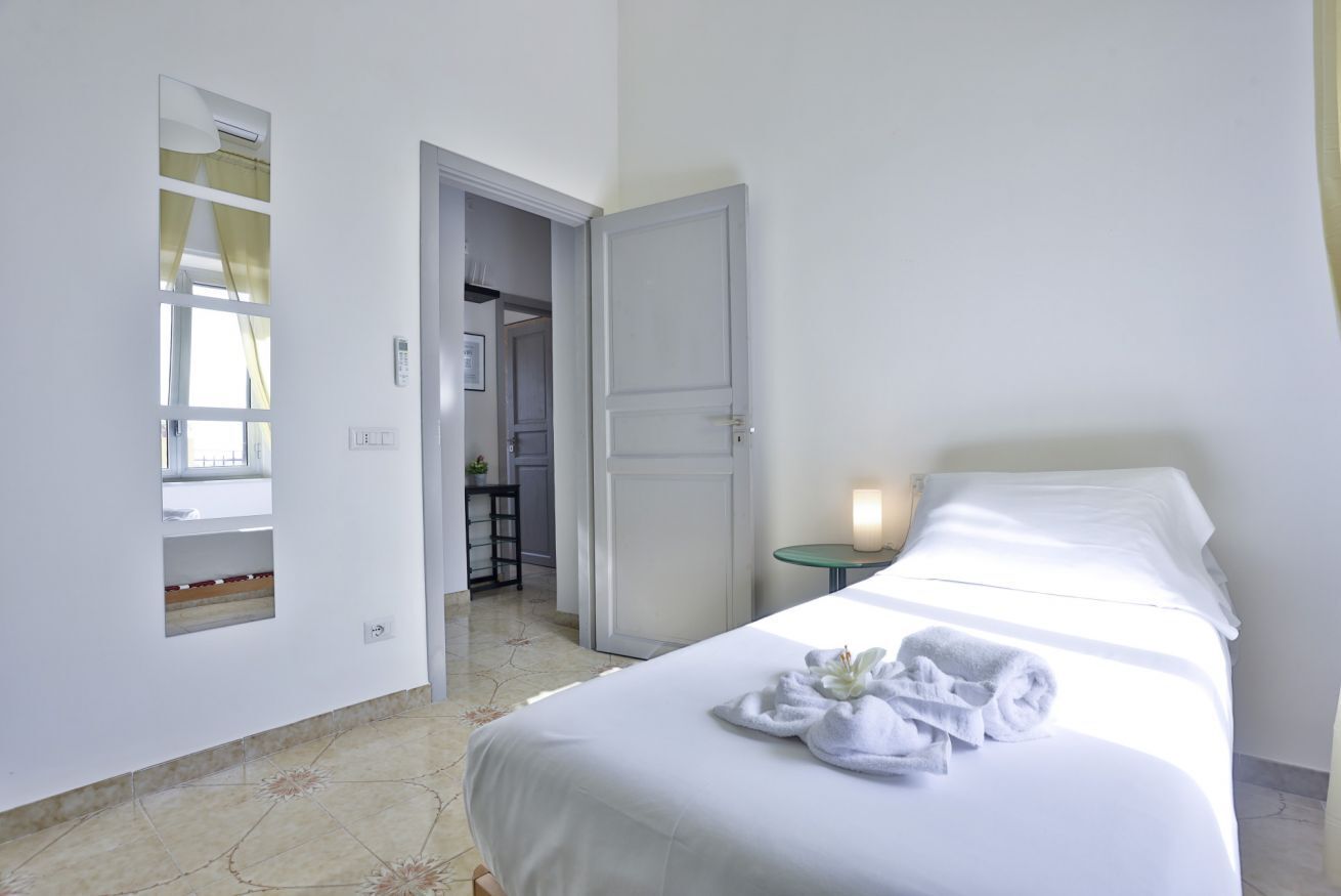 A hotel room with a bed, a bedside table with a lamp, a mirror, and a door leading to a bathroom.