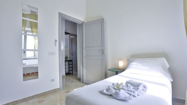 A hotel room with a bed, a bedside table with a lamp, a mirror, and a door leading to a bathroom. - GuestHost - This bright, recently renovated apartment is located in a charming 18th-century building, in a quiet and secluded location despite being in a lively and central area just steps from Via Foria and Via Cesare Rosaroll. The Cavour Metro Line 2,  (Naples)