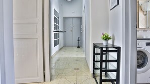 A hallway with a washing machine, a small table with a plant, and a door leading to a room. - GuestHost - This bright, recently renovated apartment is located in a charming 18th-century building, in a quiet and secluded location despite being in a lively and central area just steps from Via Foria and Via Cesare Rosaroll. The Cavour Metro Line 2,  (Naples)