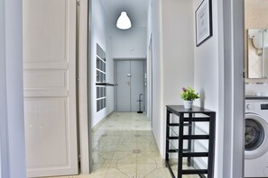 Un couloir avec un lave-linge, une petite table sur laquelle est posée une plante, et une porte qui donne sur une pièce.