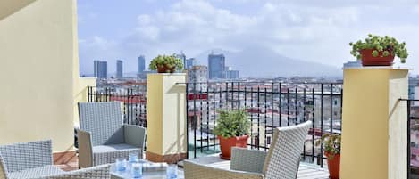 A balcony with wicker furniture, potted plants, and a cityscape view.