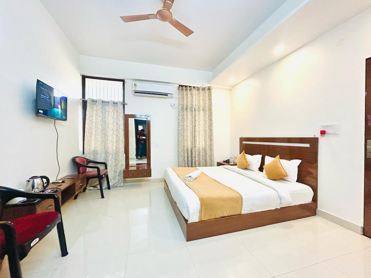 A hotel room with a bed, a desk, a chair, a television, and a ceiling fan.