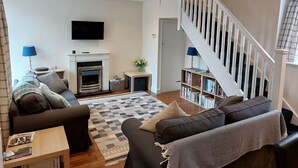 A living room with a fireplace, sofa, bookshelf, and a staircase. - The Coach House- Canonbie (Canonbie)