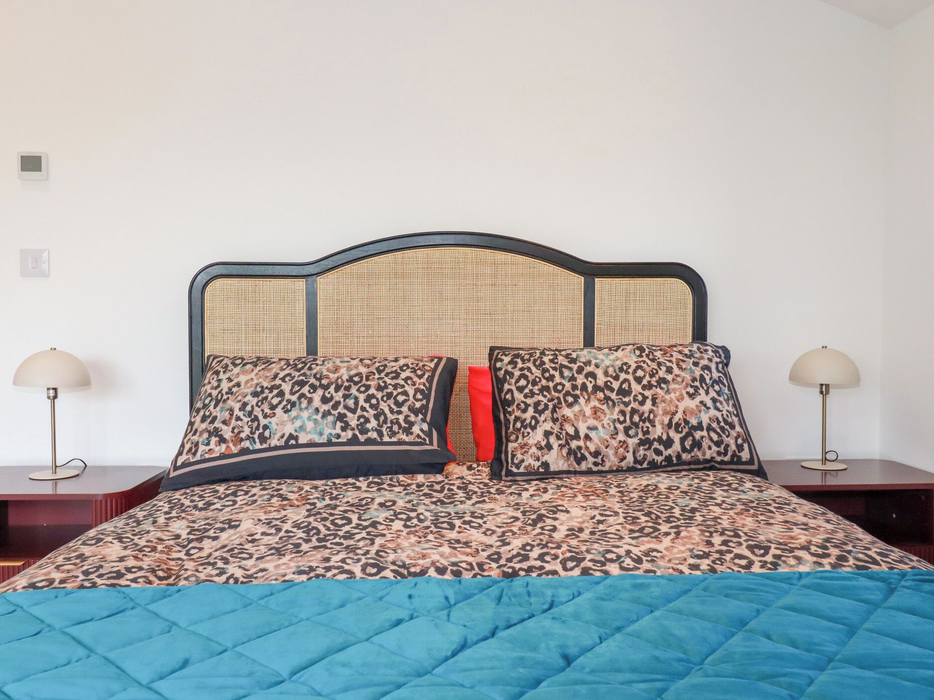 A bed with a blue quilt, two leopard print pillows, and a headboard with a woven pattern.
