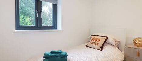A bedroom with a bed, a window, a bedside table, and a nightstand.