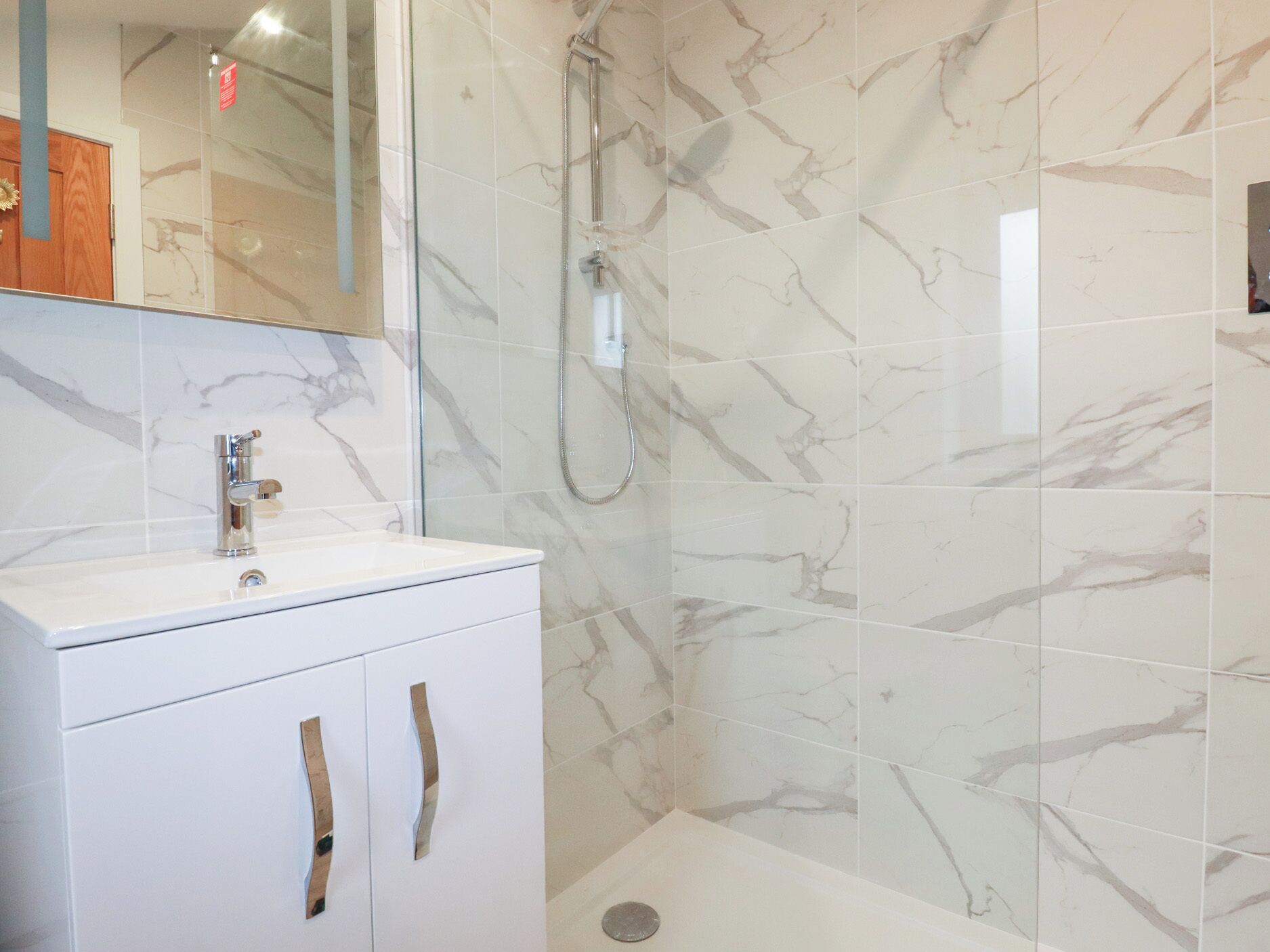 A bathroom with a white marble shower, a white sink with a modern faucet, and a cabinet with two handles.