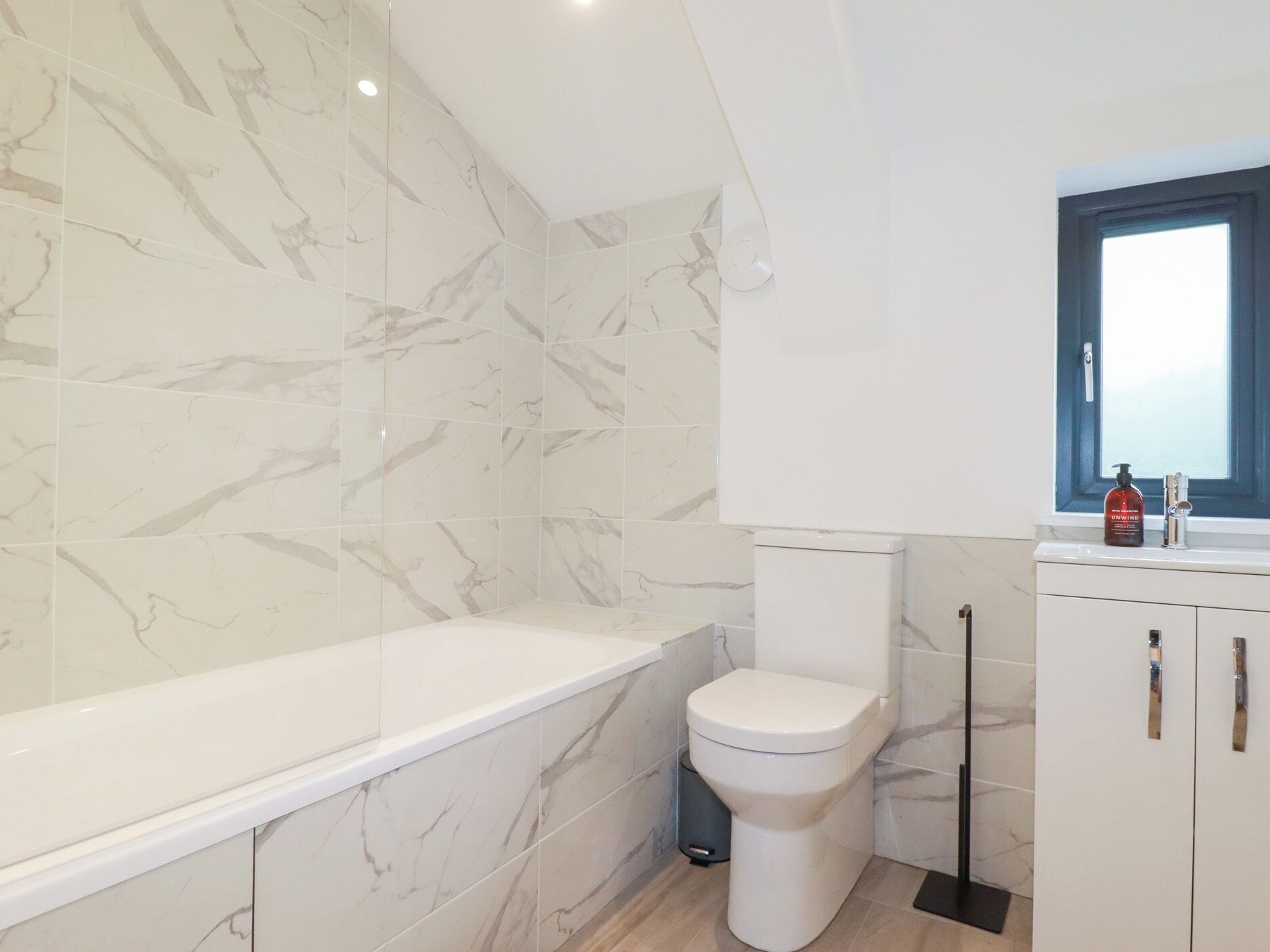 Ein modernes Badezimmer mit Marmorwand, einer weißen Badewanne, einer Toilette und einem Fenster mit Blick.