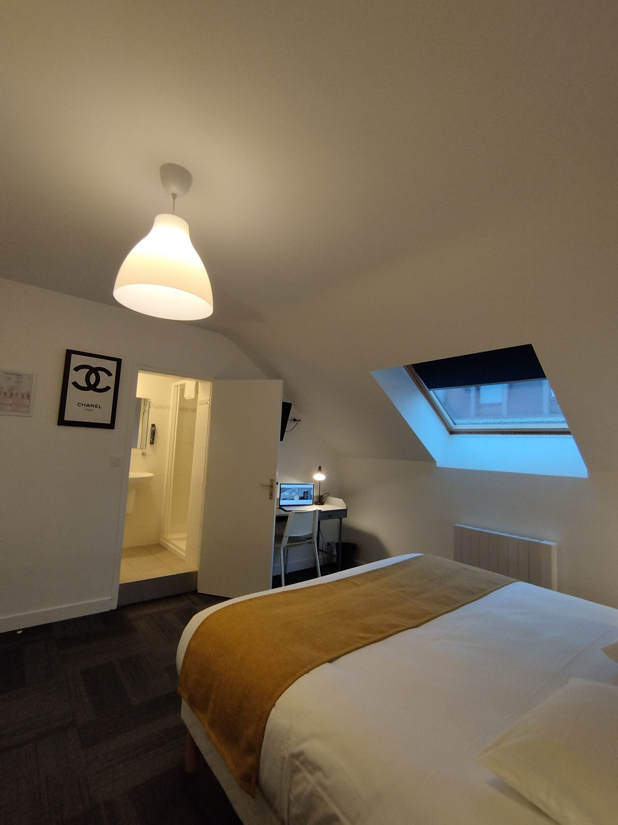 A bedroom with a bed, a desk with a computer, a window, and a door leading to a bathroom.