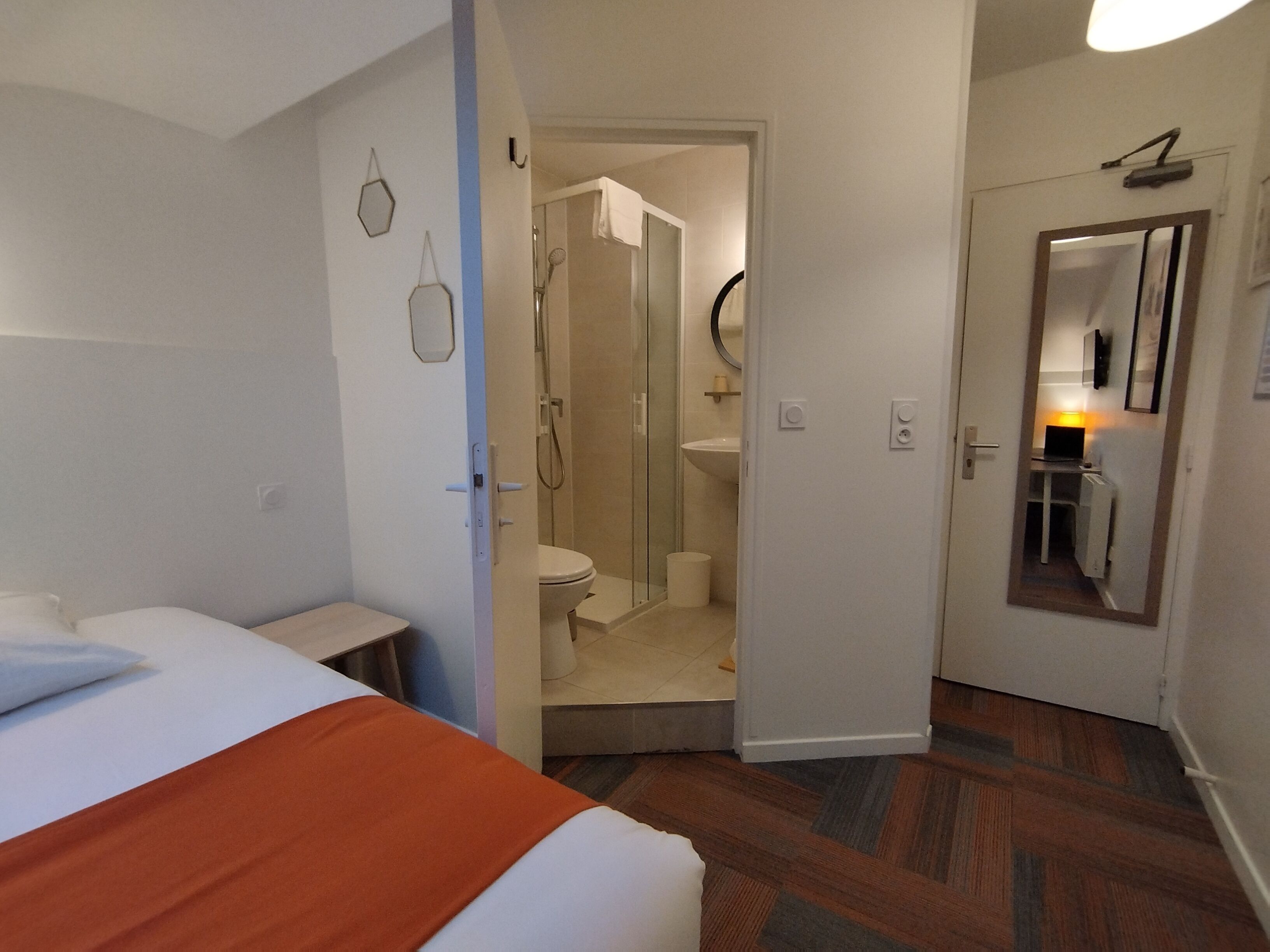Ein Hotelzimmer mit Bett, Nachttisch, Duschbereich, Waschbecken und Spiegel.