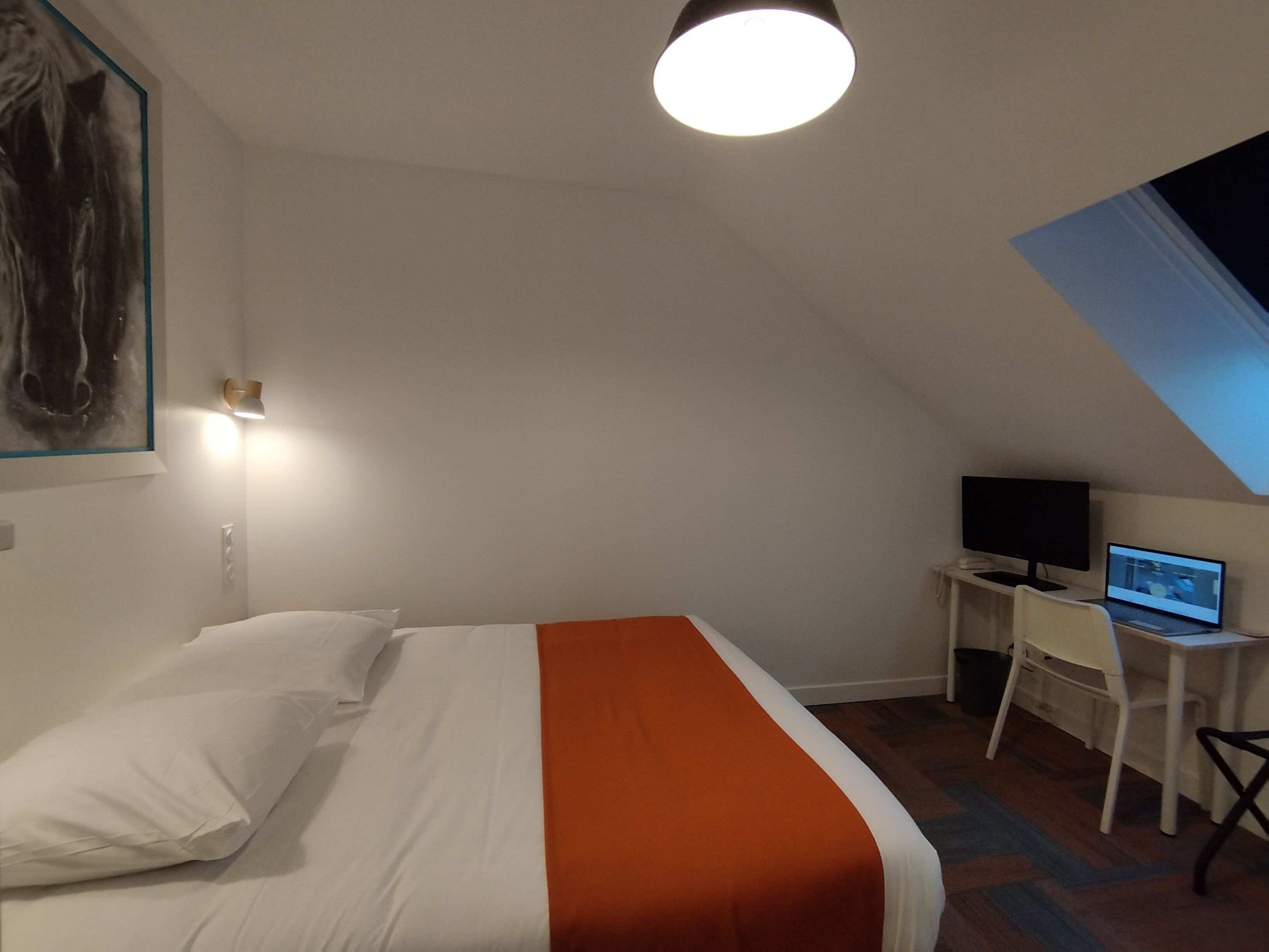 Un dormitorio con una cama, un escritorio con una computadora y un cuadro en la pared.