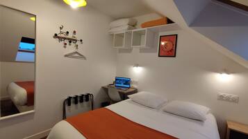 A bedroom with a bed, a desk with a laptop, a hanging light fixture, a clock, and a mirror.