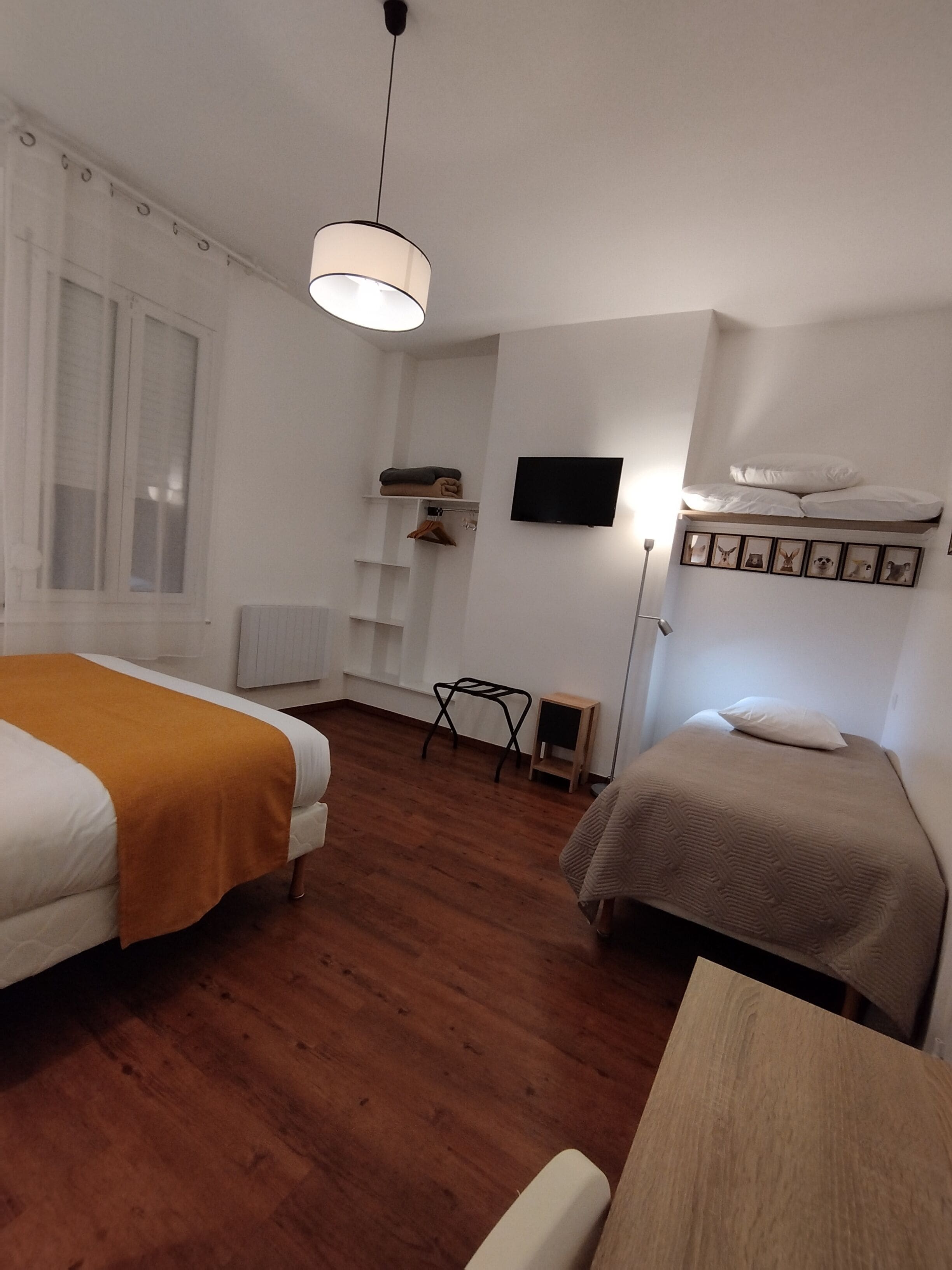 Een kamer met twee bedden, een houten vloer, een aan de muur bevestigde televisie en een raam met jaloezieën.