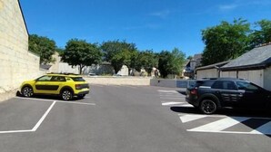 A parking lot with two cars, a yellow car on the left and a black car on the right, under a clear blue sky. - The Originals Access Hotel Le Canter (Saumur)