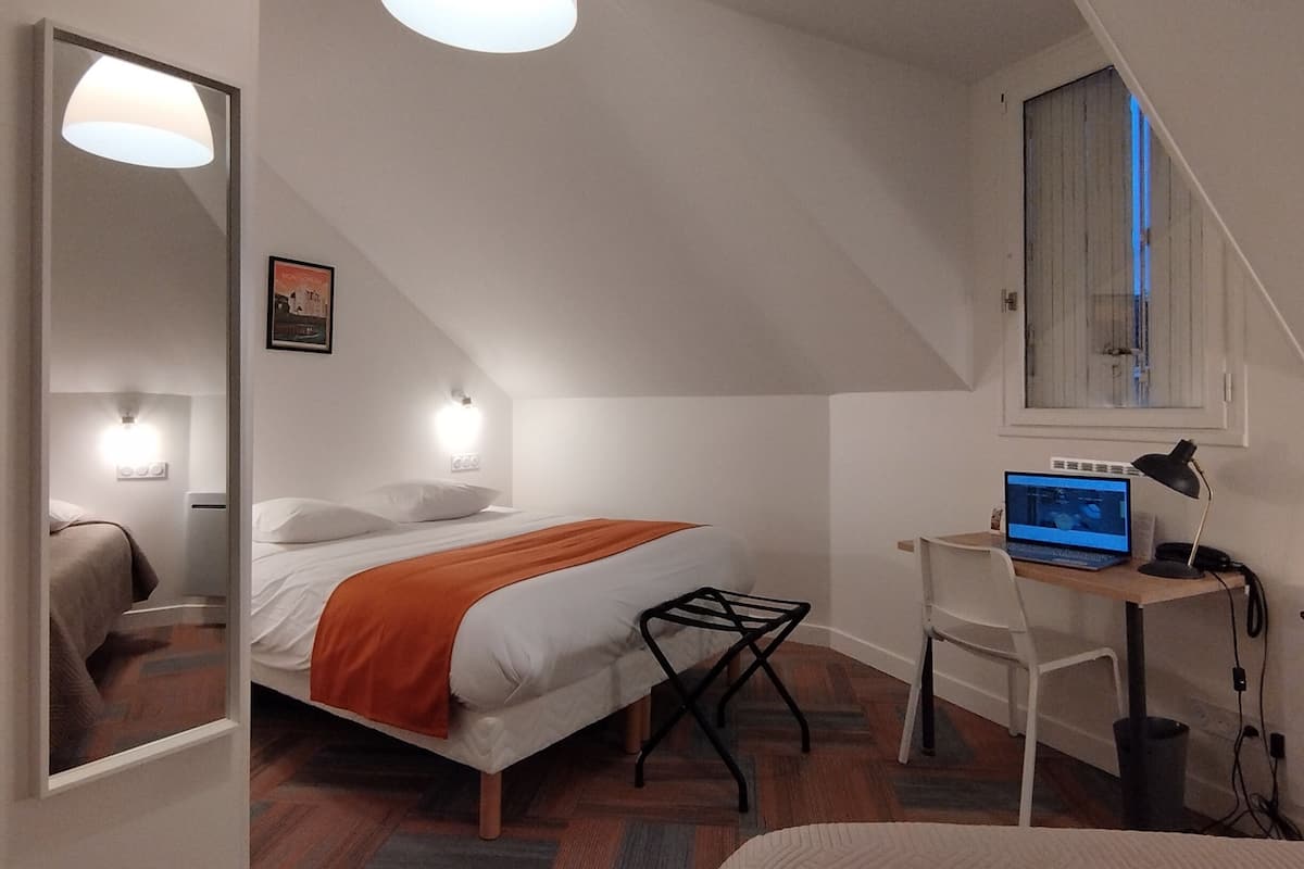 Un dormitorio con cama, escritorio, silla, espejo y lámpara colgante.