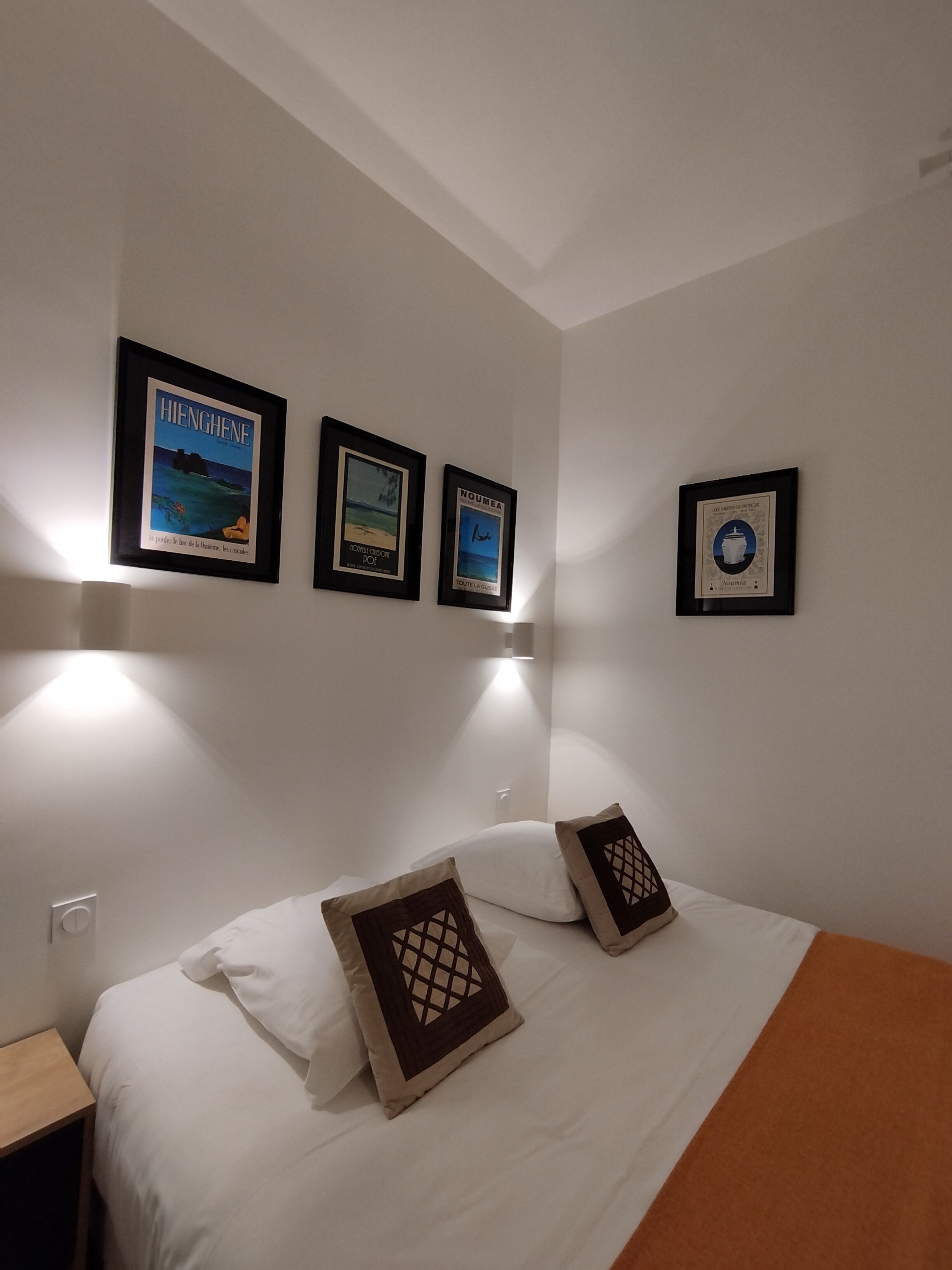 Une chambre d’hôtel avec un lit, deux oreillers et trois tableaux encadrés accrochés au mur.
