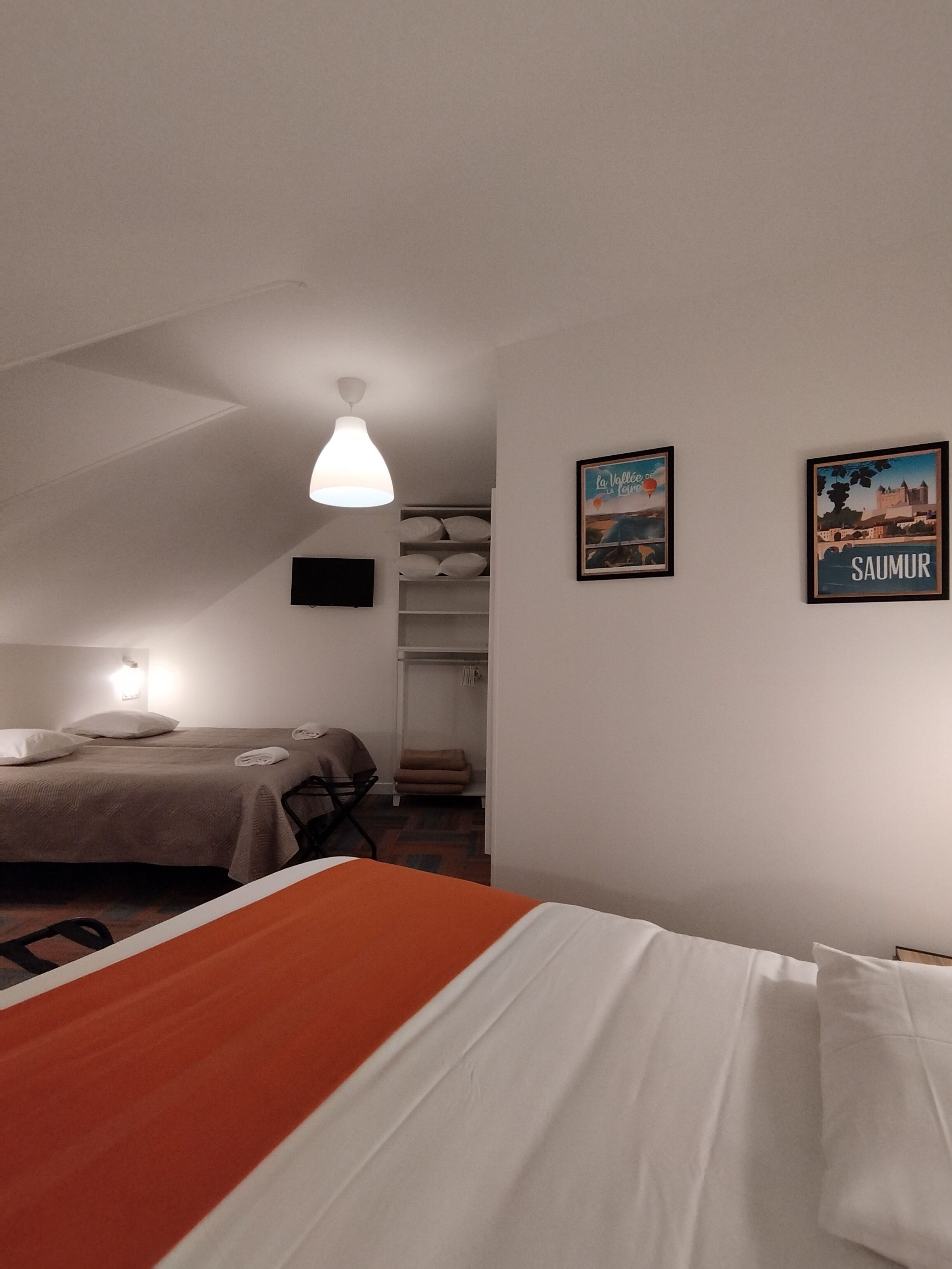 Een hotelkamer met twee bedden, een kast en twee ingelijste foto’s aan de muur.