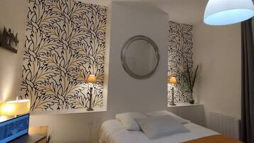 Een hotelkamer met een bed, een bureau met een laptop, een ronde spiegel en een muur met een bladmotief.