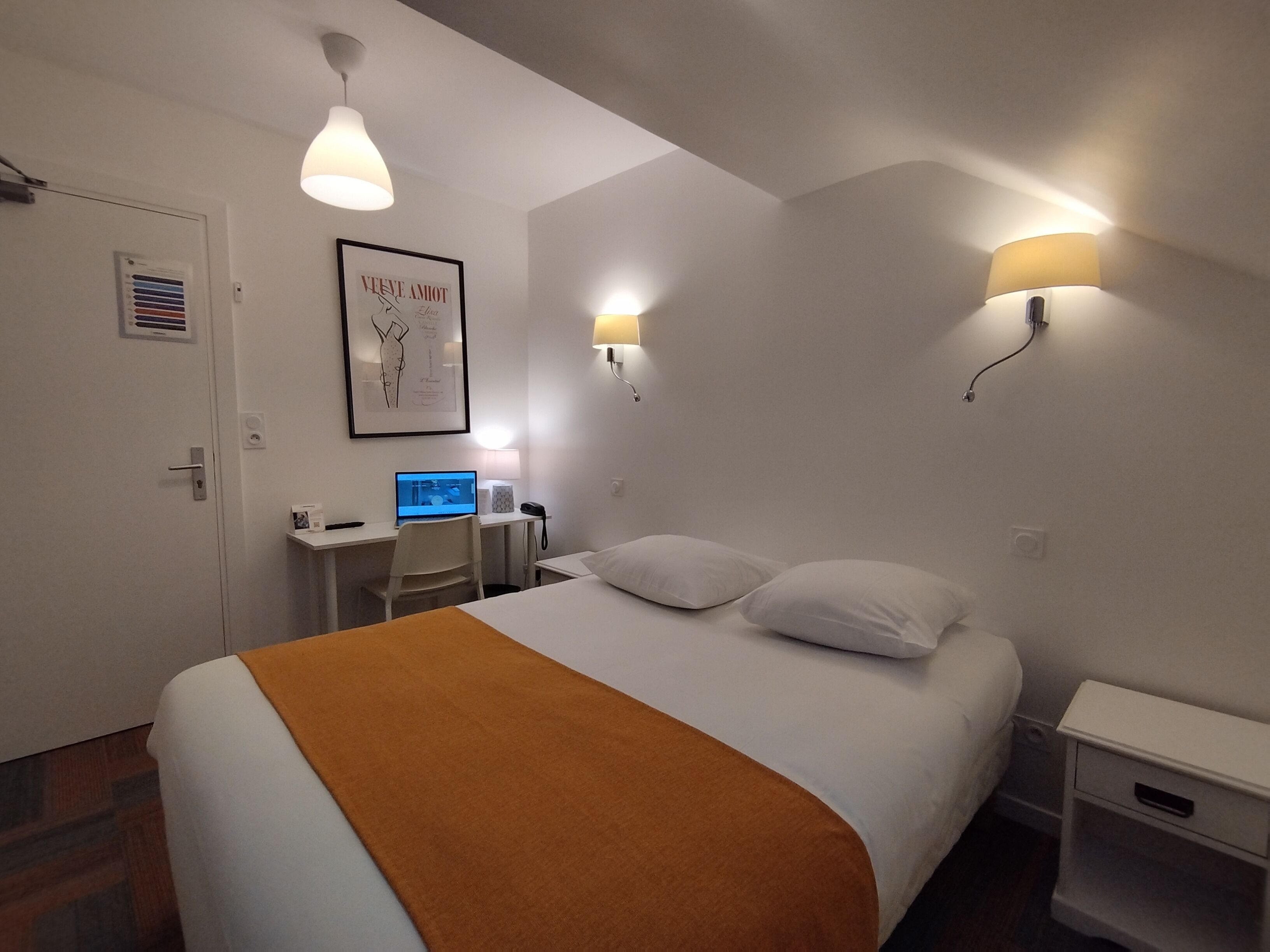 Ein Hotelzimmer mit einem Bett, einem Schreibtisch mit Computer, einem Sessel und zwei Wandlampen.