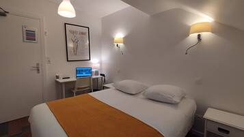 Ein Hotelzimmer mit einem Bett, einem Schreibtisch mit Computer, einem Sessel und zwei Wandlampen.