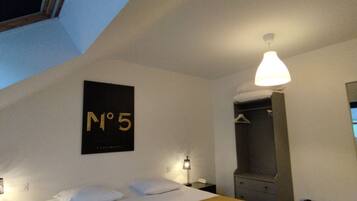 Habitación de hotel con cama, mesita de noche, lámpara, perchero y cartel en la pared.