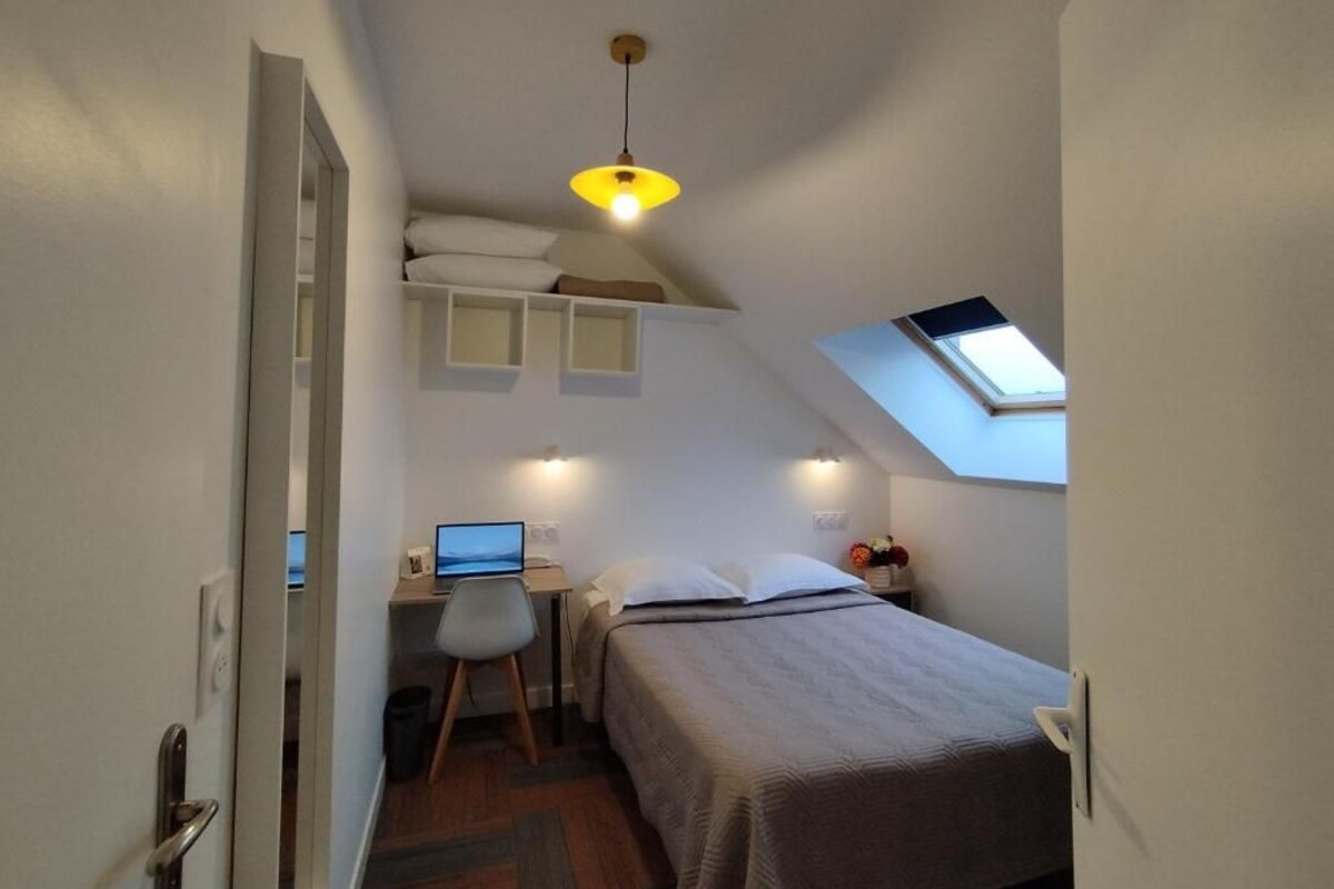Une chambre à coucher de taille réduite, avec un lit superposé, un bureau avec un ordinateur portable et une lucarne.