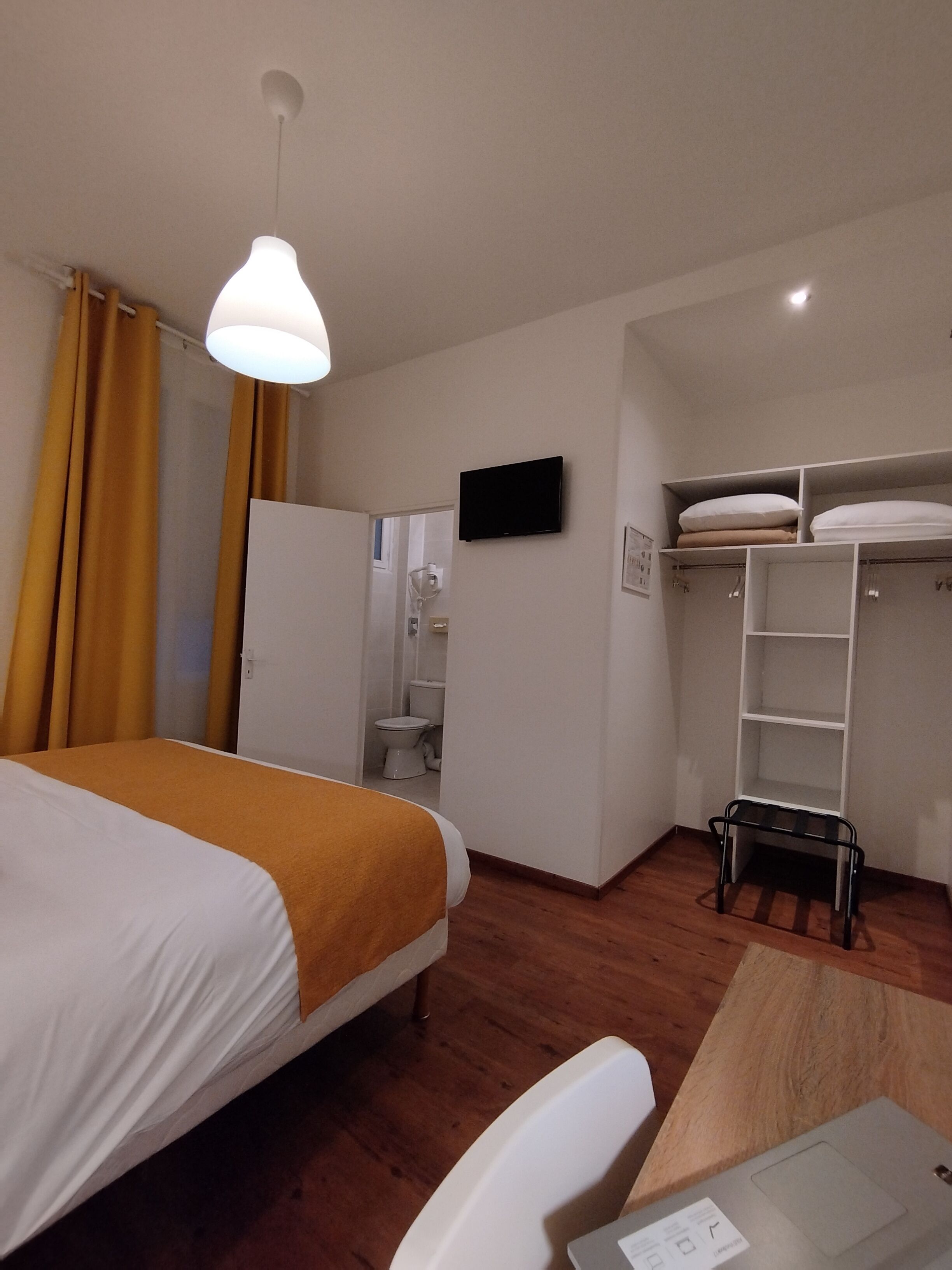 A hotel room with a bed, a desk, a chair, a wardrobe, and a television.