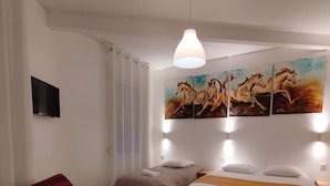 A hotel room with a bed, a desk with a laptop, a red armchair, and a painting of horses on the wall. - The Originals Access Hotel Le Canter (Saumur)