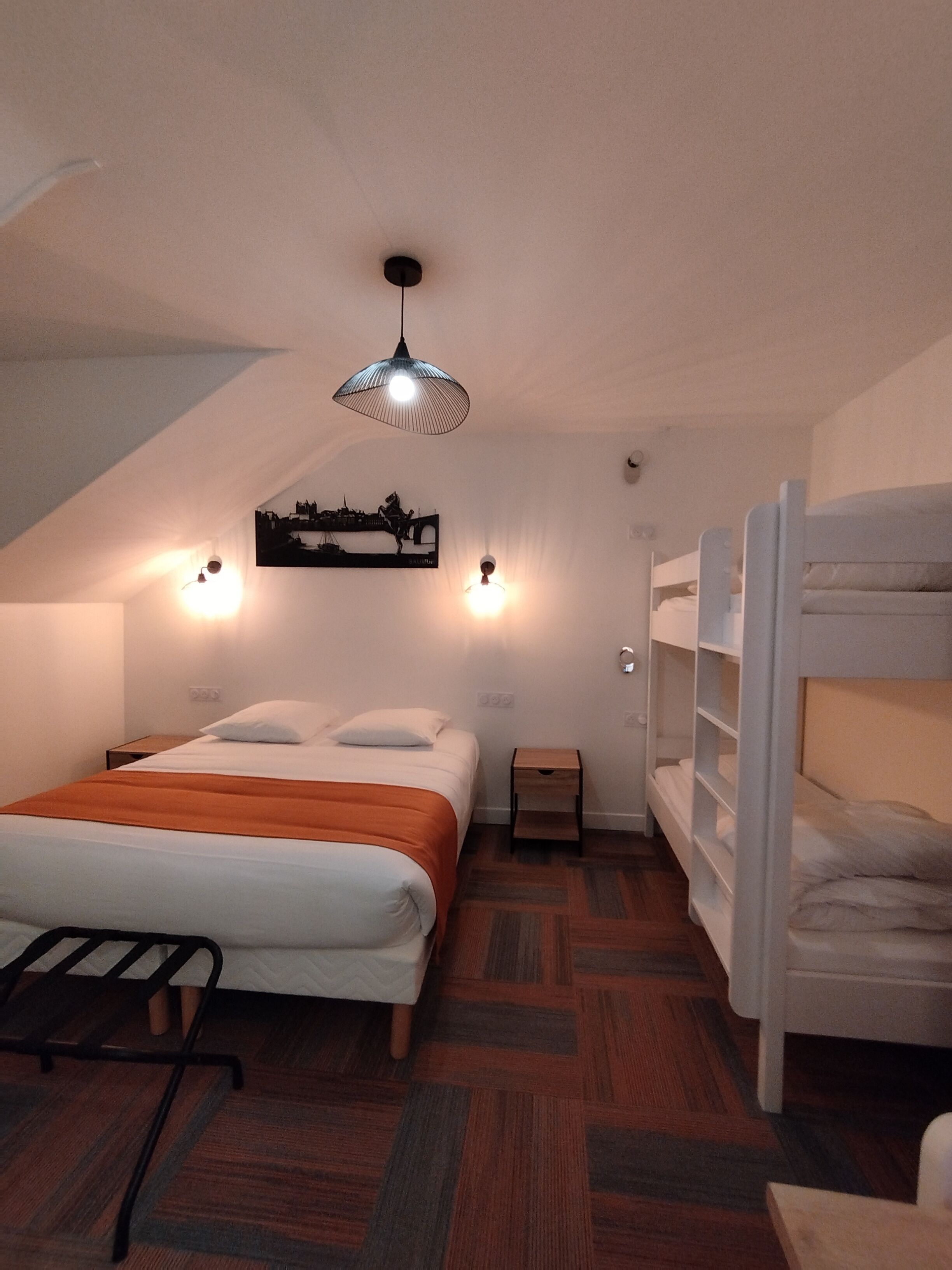 Ein Schlafzimmer mit einem Bett, zwei Stockbetten, einer Hängeleuchte, einem Wandbild und einem kleinen Nachttisch.