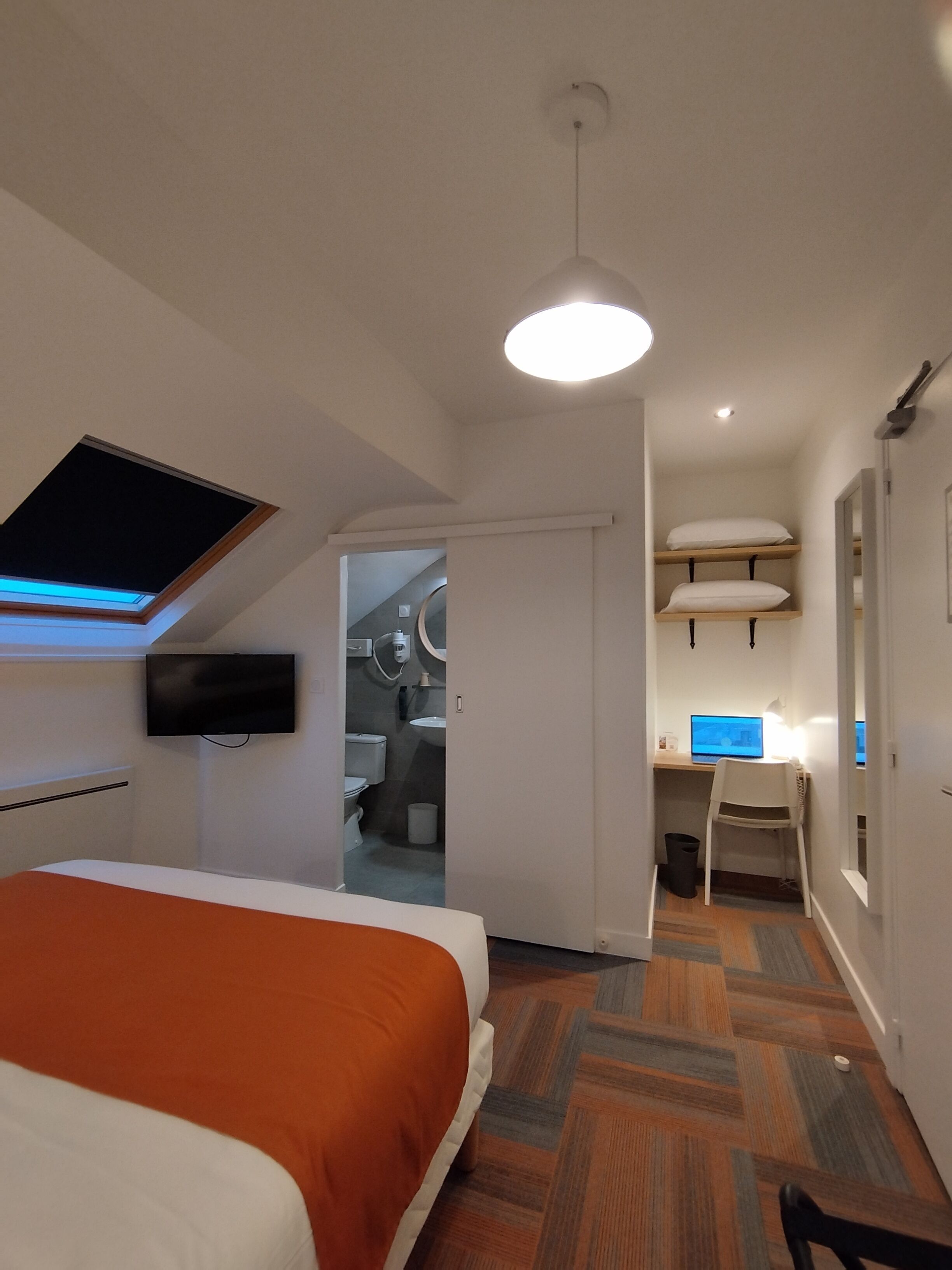 A modern hotel room with a bed, a desk, a chair, and a television.