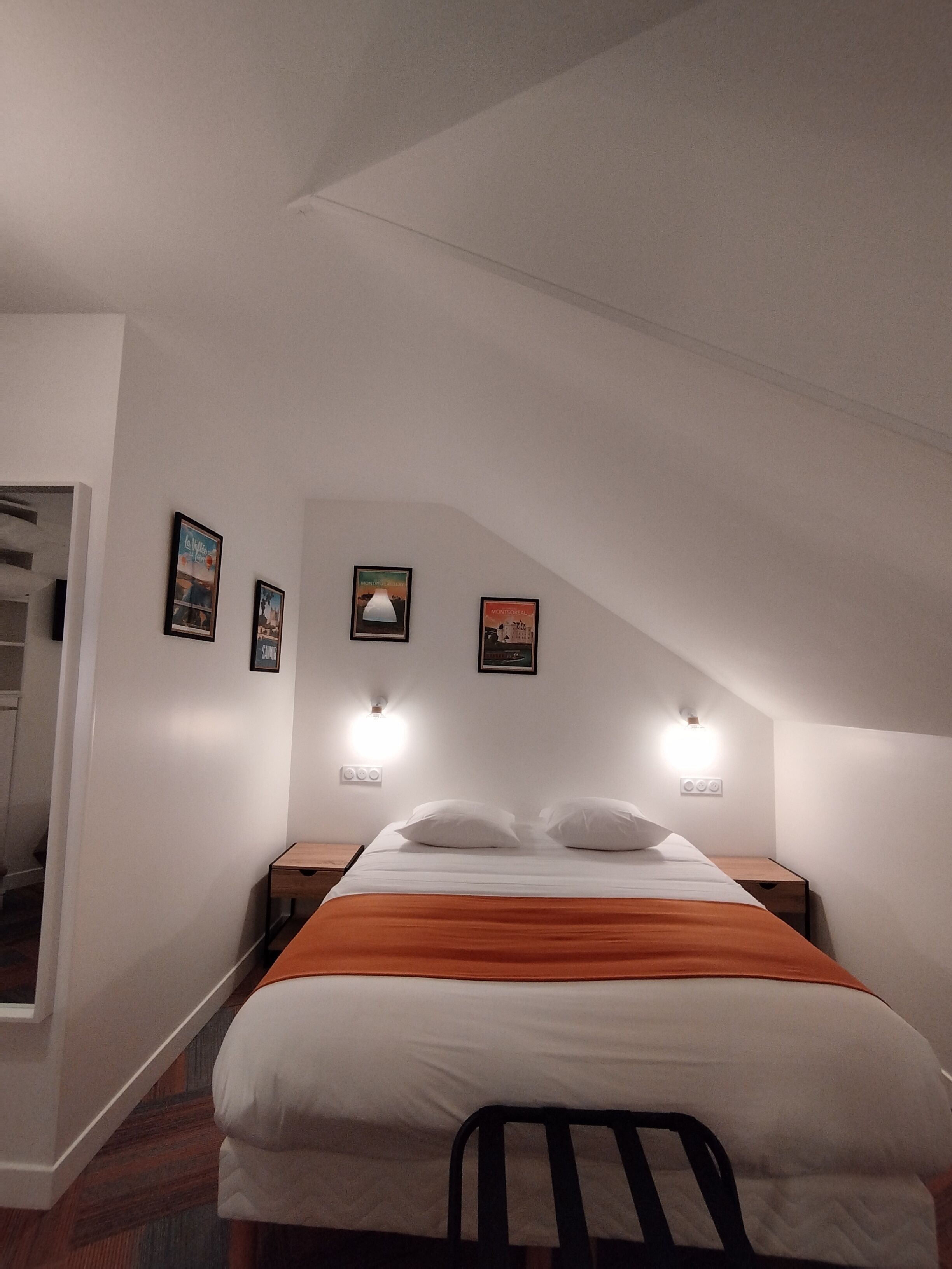 Une chambre à coucher comprenant un lit, deux tables de chevet, une commode et trois lampes fixées au mur.