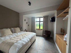 A bedroom with a large bed, a chair, a TV, and a window with curtains.