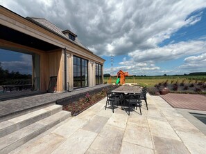 A modern house with a patio, a dining table, and a playhouse.