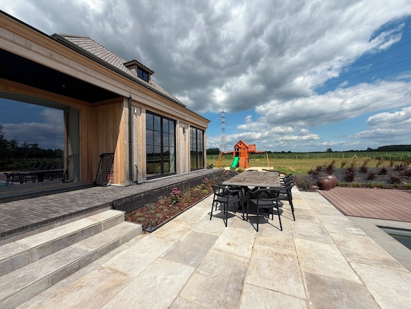 A modern house with a patio, a dining table, and a playhouse.