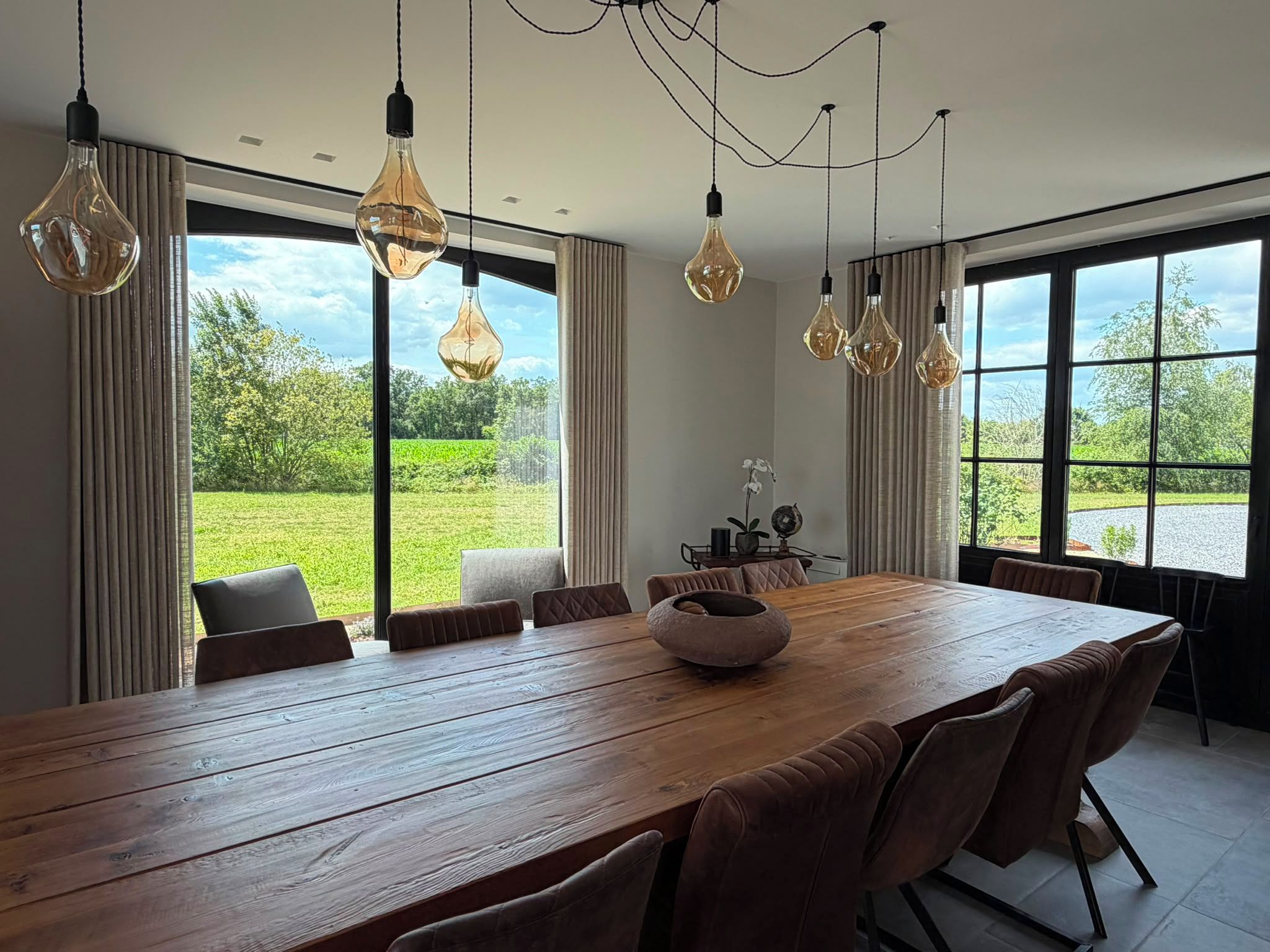 A dining area with a wooden table, multiple chairs, and hanging light fixtures.
