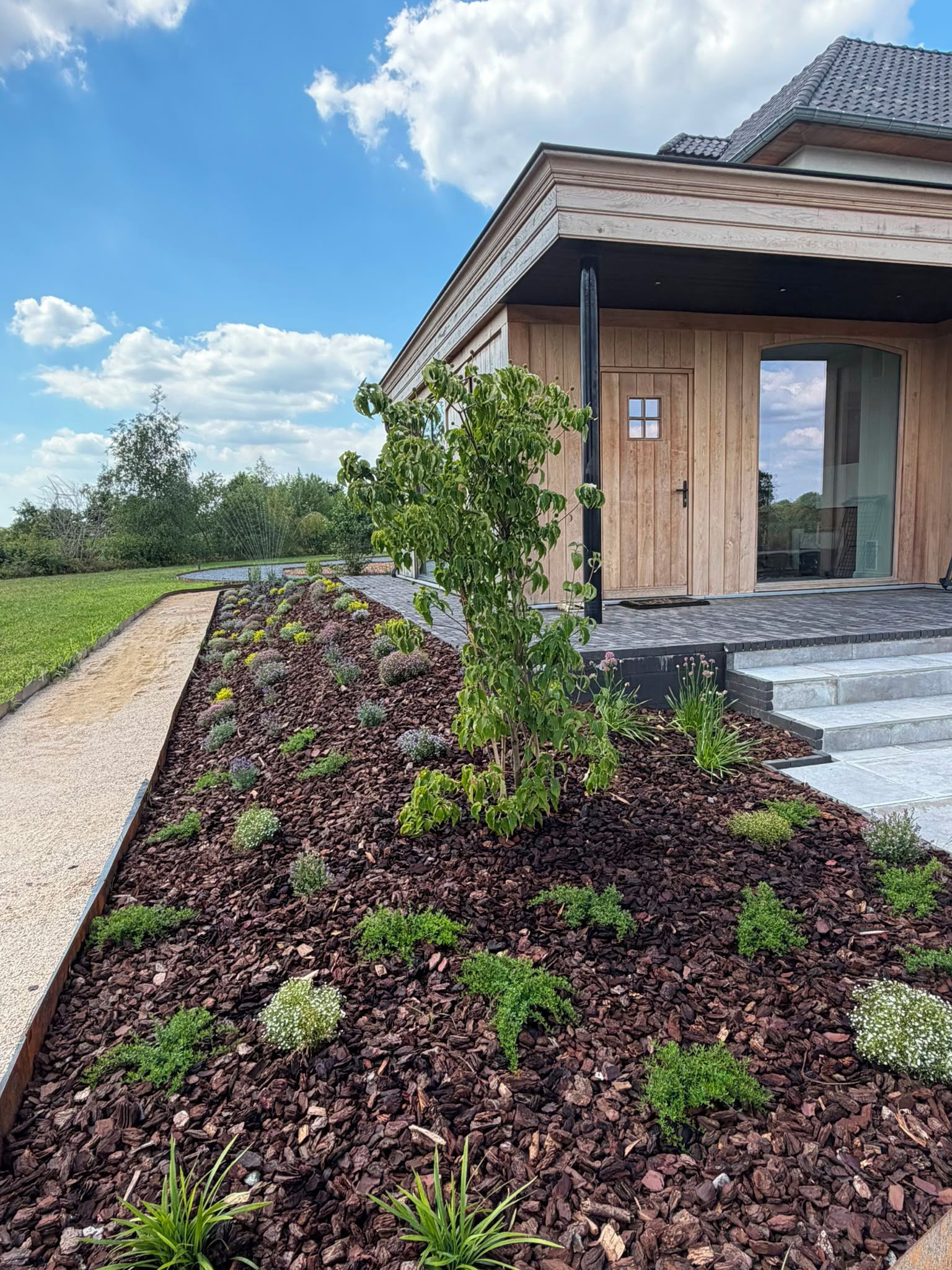 Ein modernes Haus mit einem angelegten Garten, der Mulch und verschiedene Pflanzen zeigt.