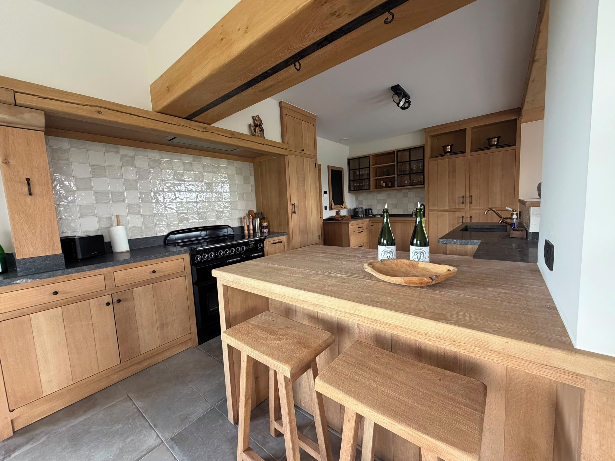 A modern kitchen with wooden cabinets, a central island with bar stools, and a tiled backsplash.