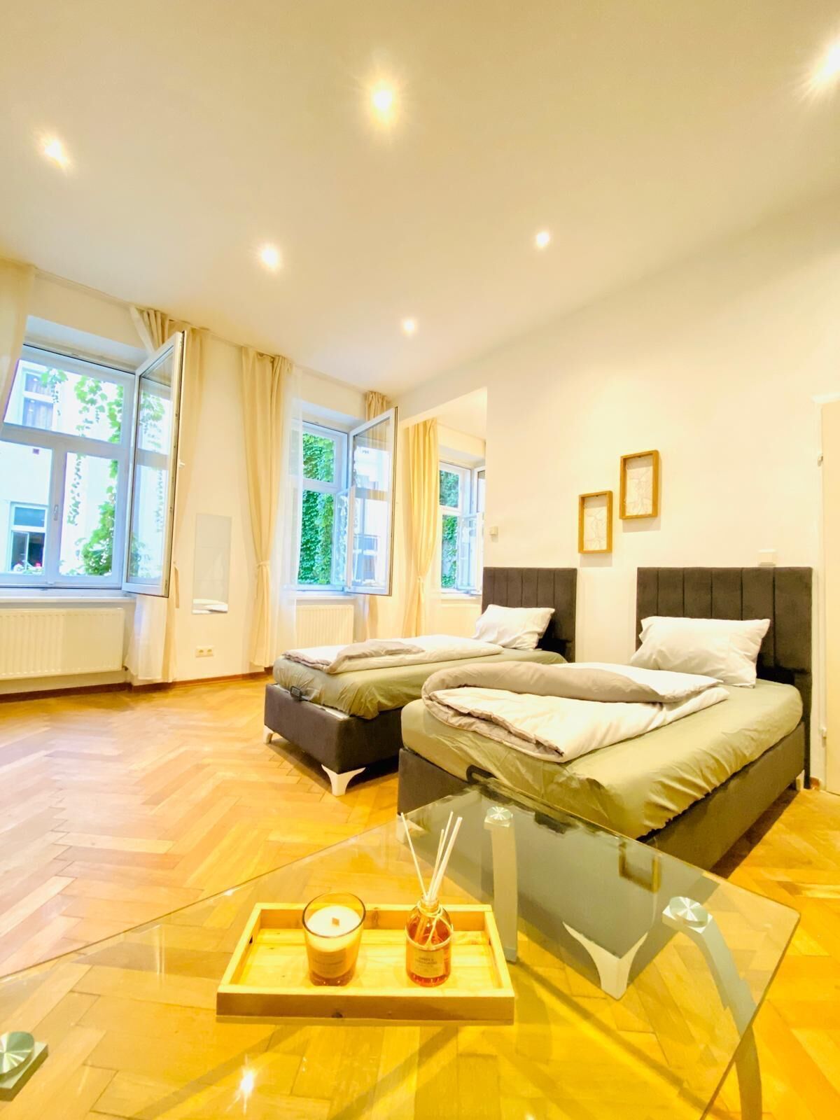 Ein modernes Hotelzimmer mit zwei Betten, großen Fenstern, einem Glastisch mit Kerzen und Blick auf Grünflächen.