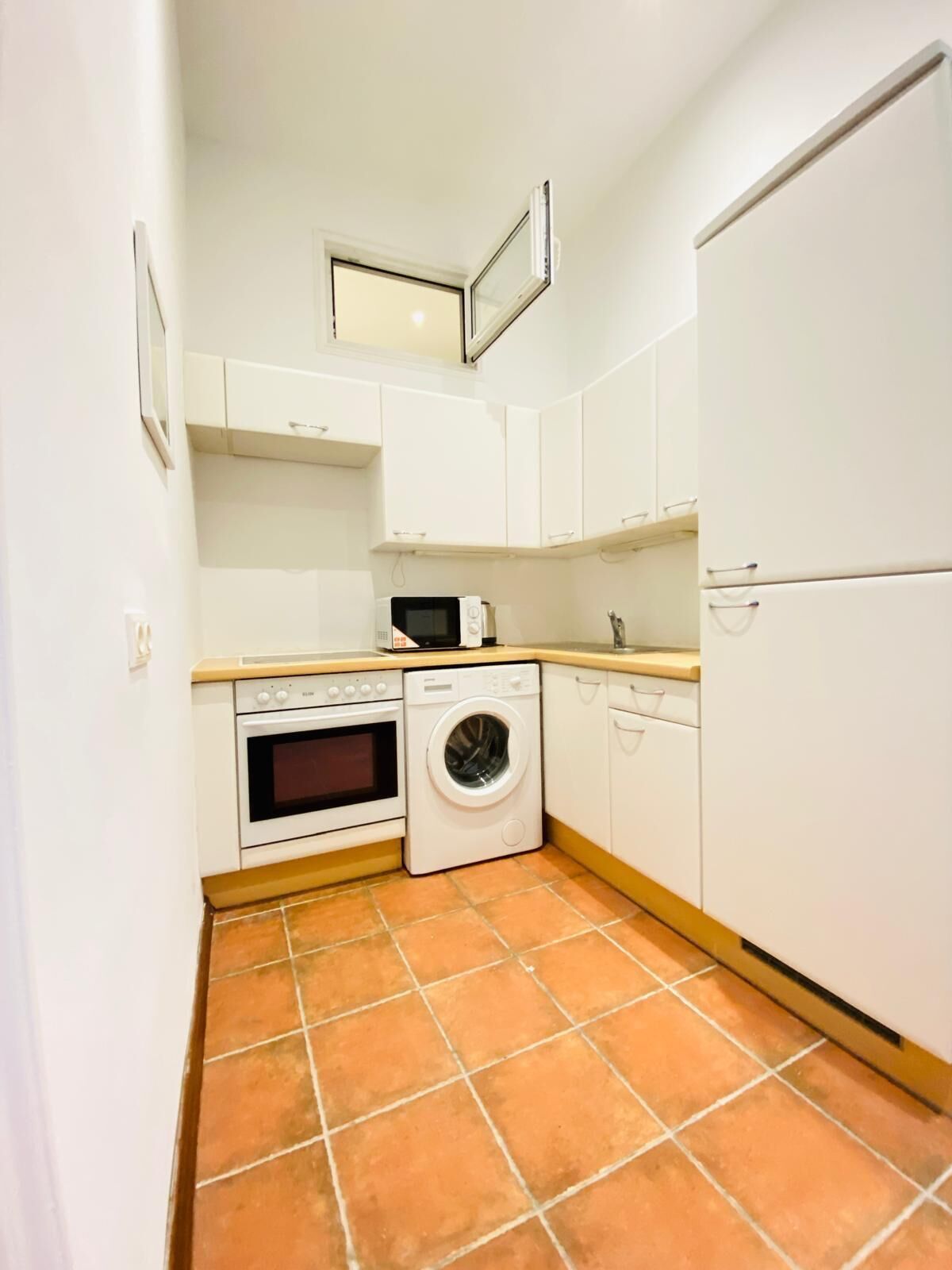 A compact kitchen with white cabinets, a washing machine, an oven, and a microwave.