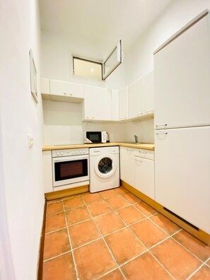 Une cuisine de taille réduite avec des meubles blancs, un lave-linge, un four et un four à micro-ondes.
