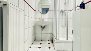 Un baño con azulejos blancos, lavabo, espejo, ducha y radiador.