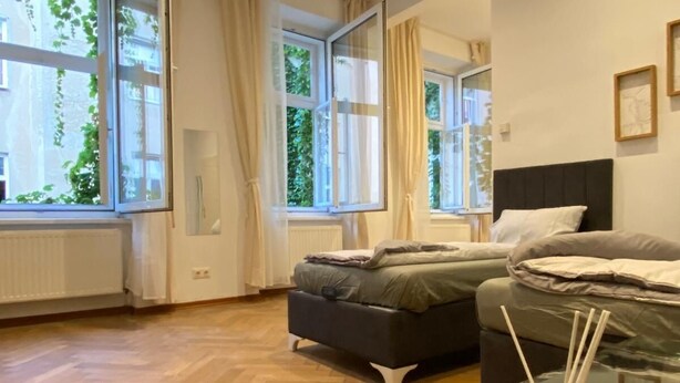 Un dormitorio moderno con dos camas, ventanas amplias y una mesa de centro de vidrio con una vela y difusor de aroma.