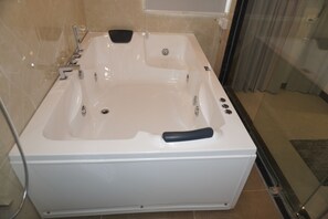 A large, rectangular bathtub with a black handle, a handheld showerhead, and a built-in seat. - Hotel Blesskey (Jaipur)