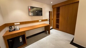 A hotel room with a wooden desk, a television mounted on the wall, a minibar, and a wardrobe. - Hotel Blesskey (Jaipur)