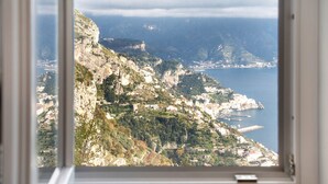 Blick aufs Meer durch ein Fenster, der eine zerklüftete Klippe, eine kleine Siedlung und ein Gewässer zeigen.