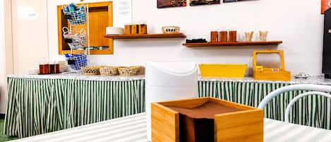 Una habitación con cortinas verde y blanco a rayas, una estación de café con cestas y tazas, y una pared decorada con ilustraciones sobre el tema del café.