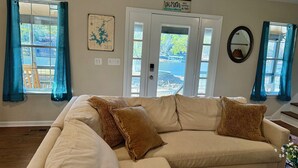 A living room with a beige sectional sofa, two blue curtains, a map on the wall, and a sign above the door. - “Just Lake Home” Wonderful 3bdrm 2bath lake front,boat ramp, dock, pet friendly (Jackson's Gap)