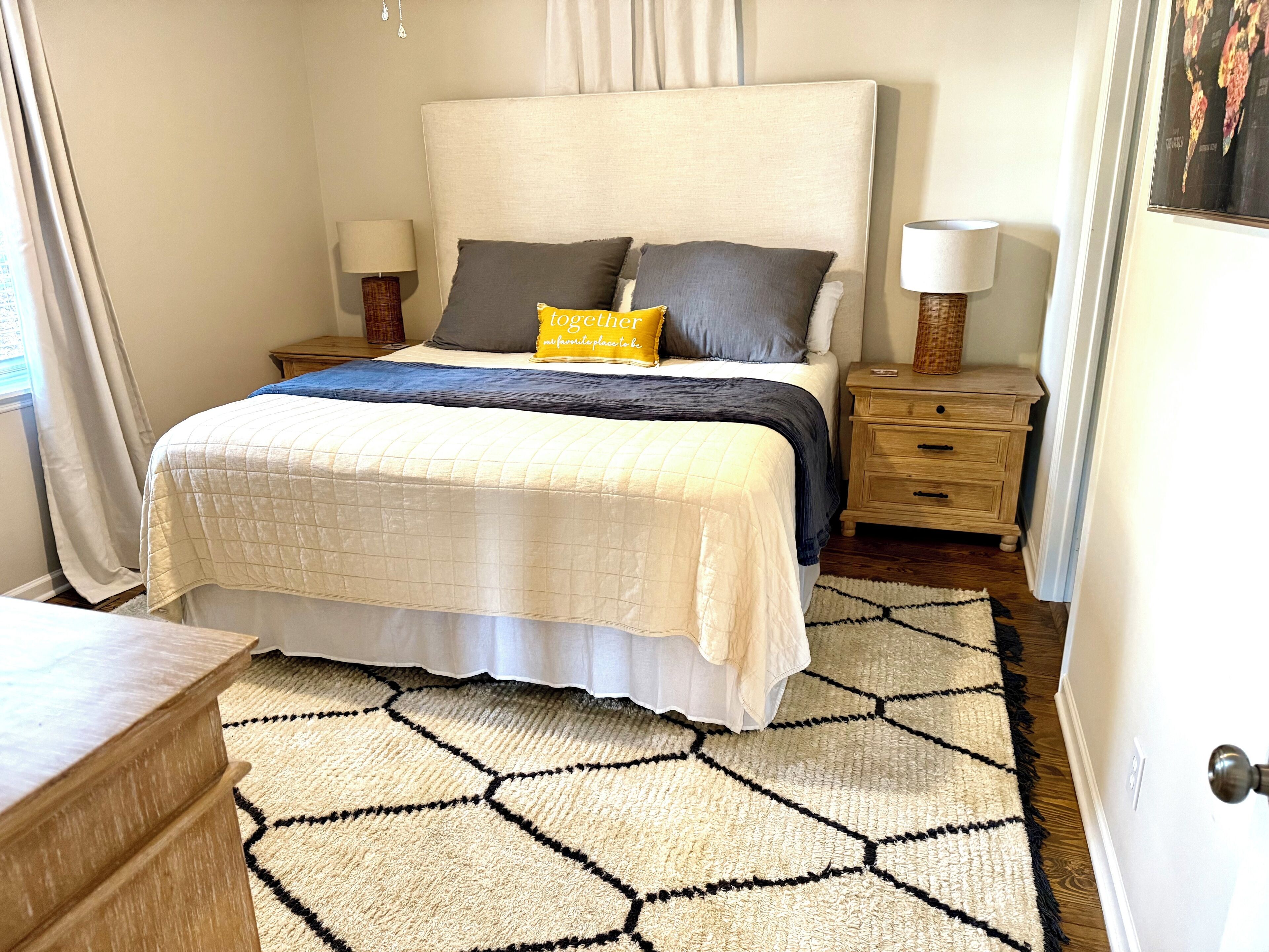A neatly arranged bedroom with a large bed, bedside tables, and a patterned rug.